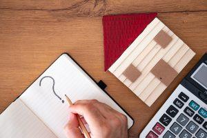 Question mark in note pad with calculator and wooden house on table.